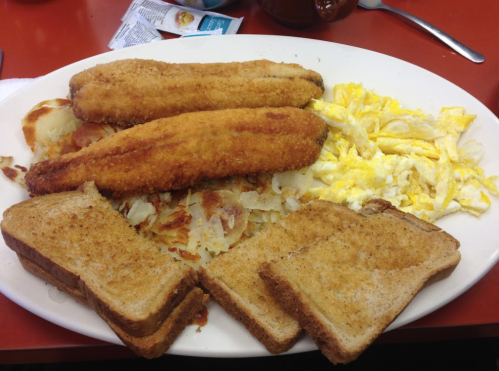 A plate of crispy fish fillets, scrambled eggs, hash browns, and slices of toasted bread.