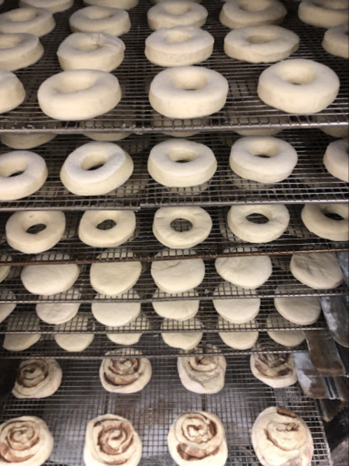 Rows of uncooked bagels and cinnamon rolls on wire racks, ready for baking.