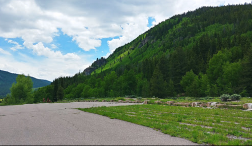 A scenic view of a green hillside with trees under a partly cloudy sky, alongside a paved area.