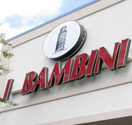 Sign for "Bambini" featuring a graphic of the Leaning Tower of Pisa, mounted on a light-colored building.