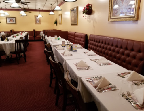 A cozy restaurant interior with neatly set tables, white tablecloths, and red upholstered seating along the walls.