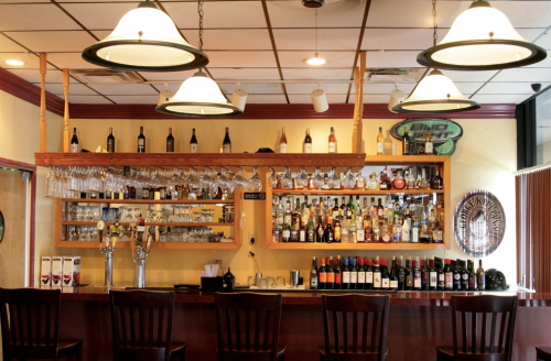 A well-stocked bar with various bottles, glasses, and bar stools in a cozy setting.