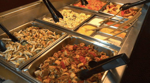 A buffet display with various pasta dishes and sauces in metal trays, served with tongs.