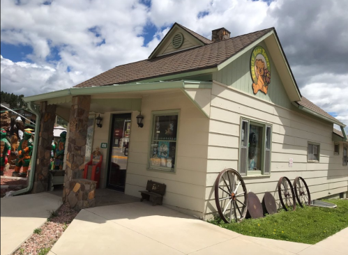 A quaint, light-colored house with a decorative lion sign, surrounded by vintage wheels and colorful statues outside.