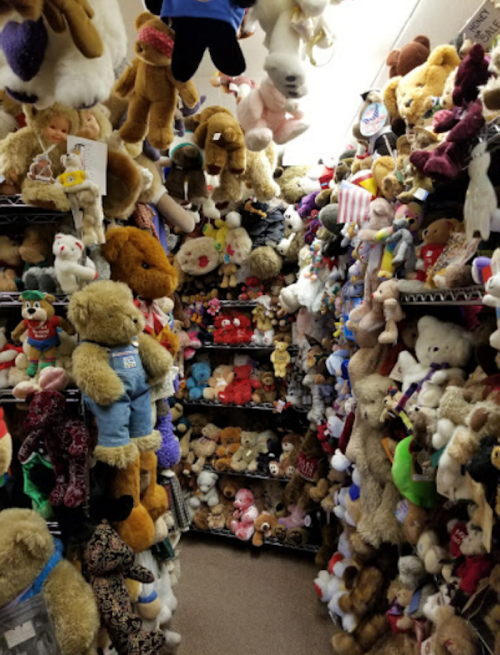 A narrow aisle filled with a dense collection of various stuffed animals and toys on shelves and hanging from above.