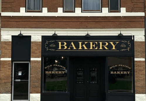 A brick building with a black and gold sign reading "Wild Prairie Bakery" above the entrance.
