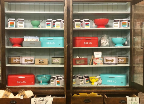 A wooden shelf displays colorful kitchen storage containers labeled "BREAD" and various bowls in teal and red.