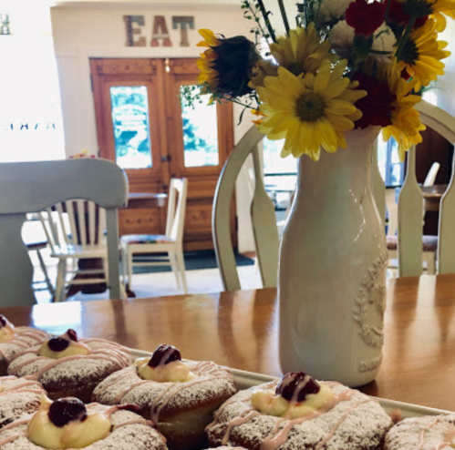 A vase of flowers beside a plate of pastries with cream and cherry topping in a cozy dining area.
