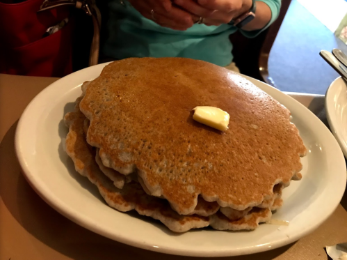 A stack of three golden-brown pancakes topped with a pat of butter on a white plate.