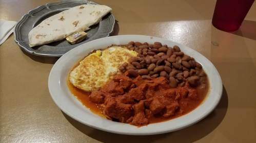A plate of food featuring eggs, beans, and meat in sauce, with a side of tortillas on a separate plate.