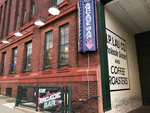 Exterior view of a brick building featuring an arcade bar sign and a wall advertising a grocery and coffee roasters.