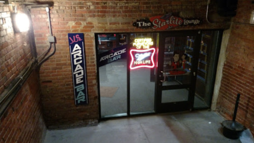 Entrance to the Starlite Lounge with neon signs for an arcade bar, featuring brick walls and a welcoming atmosphere.