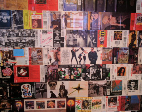 A collage of various music album covers and posters arranged on a wall, showcasing diverse artists and genres.