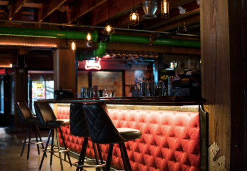 A stylish bar with a red tufted back, modern stools, and warm lighting in a rustic setting.