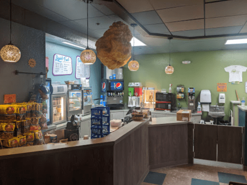 A cozy café interior with a counter, snacks, drinks, and decorative lighting.