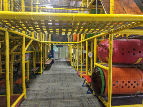Indoor playground with colorful structures, tunnels, and seating areas, enclosed by safety netting.