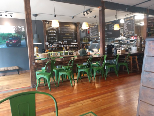 A cozy café interior with wooden floors, green chairs, and a counter displaying menu items and coffee equipment.