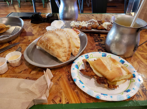 A table with two plates of food: one with stuffed flatbreads and the other with a sandwich, plus sauces and a drink.
