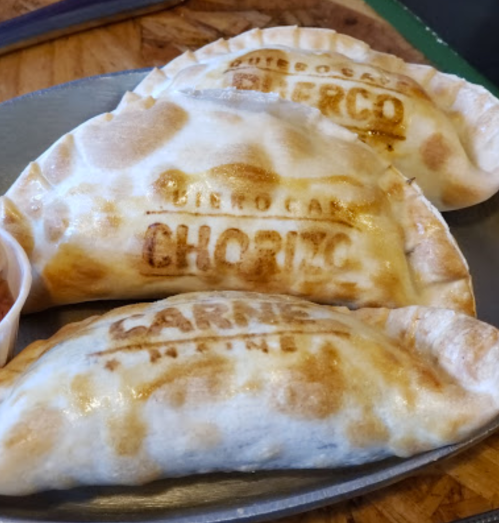 Three golden-brown empanadas with "chorizo" stamped on them, served on a metal plate.