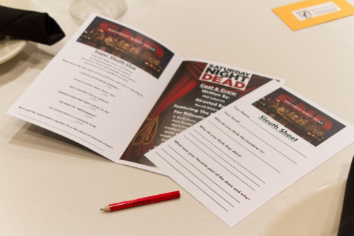Two event programs and a red pencil on a table, featuring "Saturday Night Dead" and a sleuth sheet.