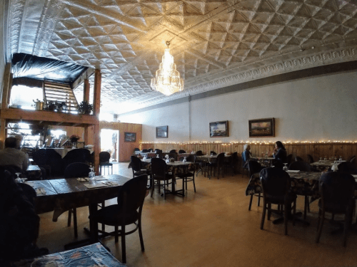 Cozy restaurant interior with wooden tables, chairs, and a chandelier, featuring soft lighting and decorative plants.