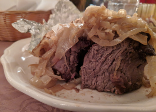 A close-up of a sliced beef dish topped with sautéed onions, served on a white plate.