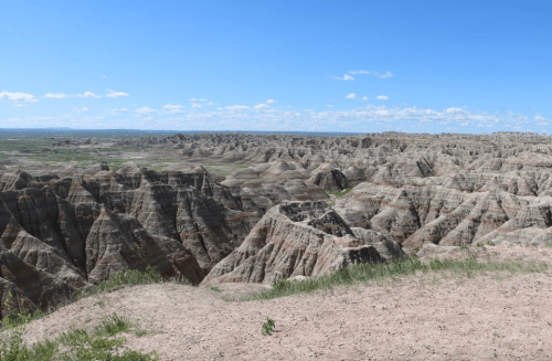 A panoramic view of rugged, layered rock formations under a clear blue sky in a vast, open landscape.