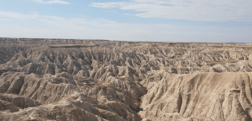 A vast, rugged landscape of eroded hills and valleys under a blue sky, showcasing natural geological formations.