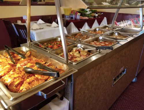 A buffet table with various dishes, including baked items, vegetables, and seafood, in a restaurant setting.