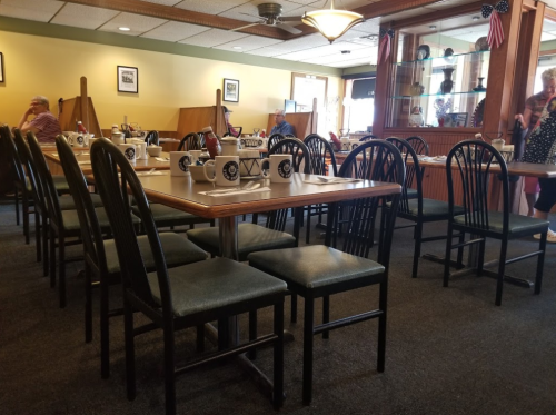 A cozy diner interior with empty tables and chairs, featuring a display case and patrons in the background.
