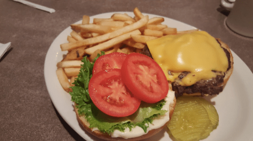 A plate with a cheeseburger topped with lettuce, tomato, and pickles, accompanied by a side of French fries.