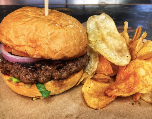 A juicy hamburger with lettuce, tomato, and onion, served with a side of crispy potato chips.
