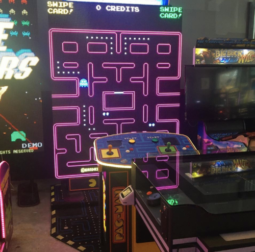 A colorful arcade setup featuring a Pac-Man game cabinet and a large screen displaying a game.