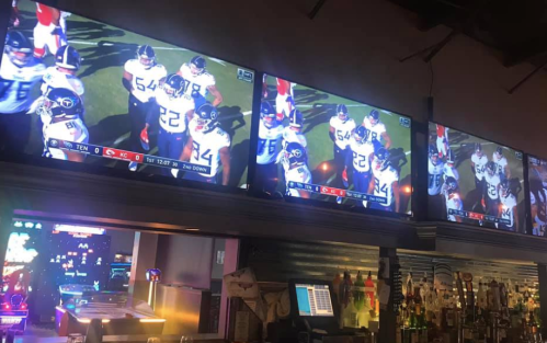 Four TVs displaying a football game, with players on the field and a scoreboard showing the teams and game details.