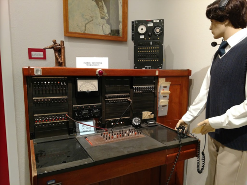 A vintage telephone switchboard with a mannequin operator, featuring various controls and a sign that says "Do Not Disturb."