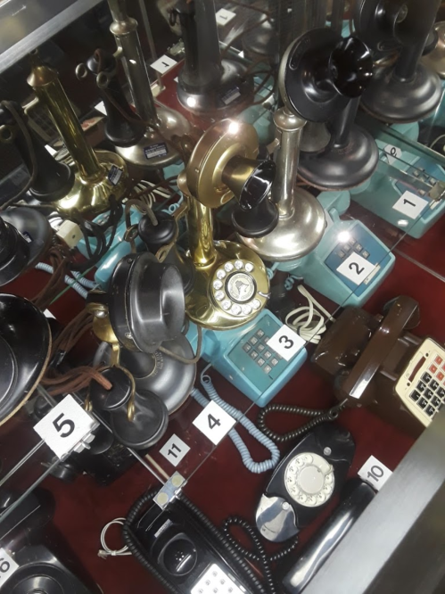 A display case filled with various vintage telephones, including rotary and modern styles, on a red background.
