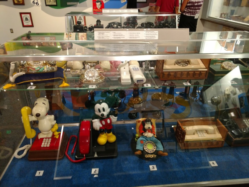Display case featuring vintage telephones, including cartoon character designs of Mickey Mouse, Snoopy, and Goofy.