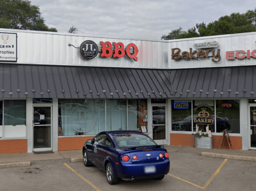 A purple car parked in front of a BBQ restaurant and a bakery with signs indicating they are open.