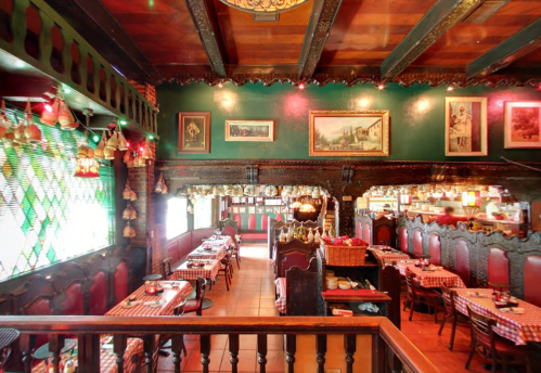 Cozy restaurant interior with wooden beams, green walls, checkered tablecloths, and warm lighting.