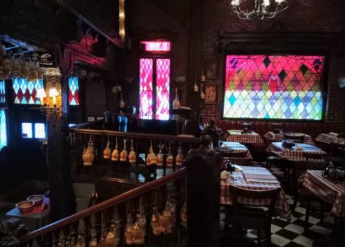 Cozy restaurant interior with stained glass windows, wooden decor, and checkered tablecloths on tables.