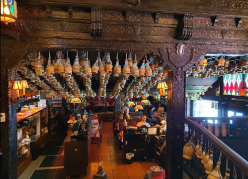 A vibrant restaurant interior with ornate wooden beams and numerous hanging lanterns, bustling with activity.