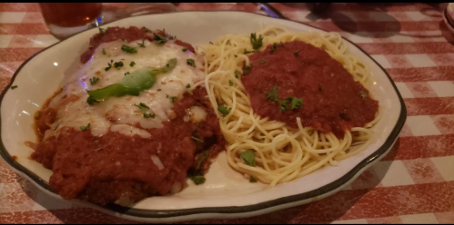 A plate of spaghetti with marinara sauce and a meat dish topped with cheese and green pepper, garnished with herbs.