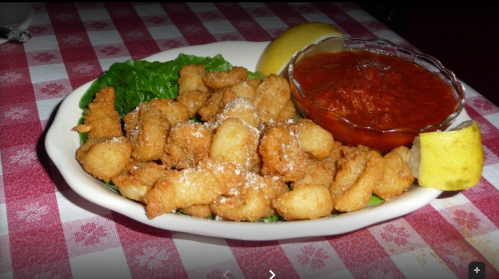 A plate of fried seafood served with lettuce, a lemon wedge, and marinara sauce on a checkered tablecloth.