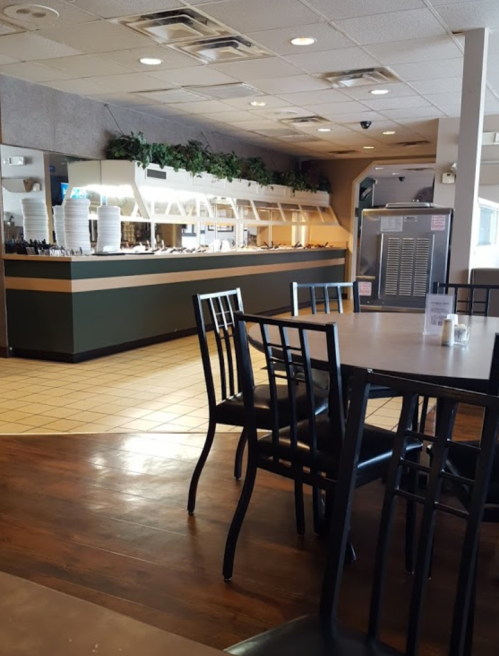 Interior of a restaurant featuring empty tables, a buffet area, and a cooler in the background.