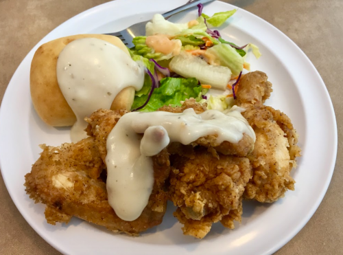 A plate of fried chicken with gravy, a biscuit, and a side salad with dressing.