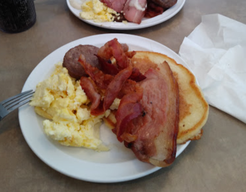 A plate of breakfast featuring scrambled eggs, bacon, sausage, and a pancake.