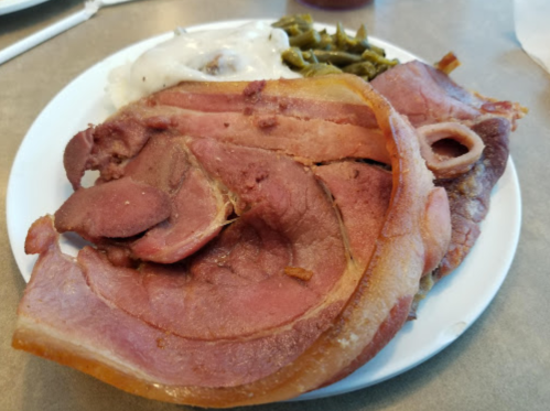 A plate of food featuring slices of ham, green beans, and a side of mashed potatoes with gravy.