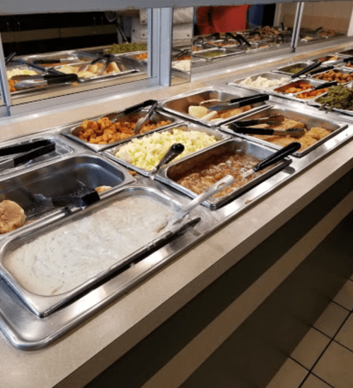 A buffet line featuring various dishes, including vegetables, mashed potatoes, and meats in metal trays.