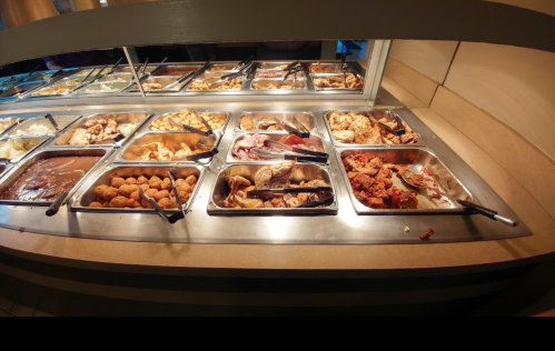 A buffet display featuring various dishes in metal trays, including meats, sides, and desserts.