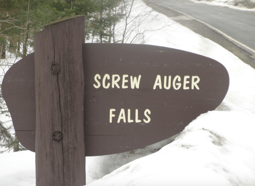 Sign for Screw Auger Falls, set against a snowy landscape near a road.